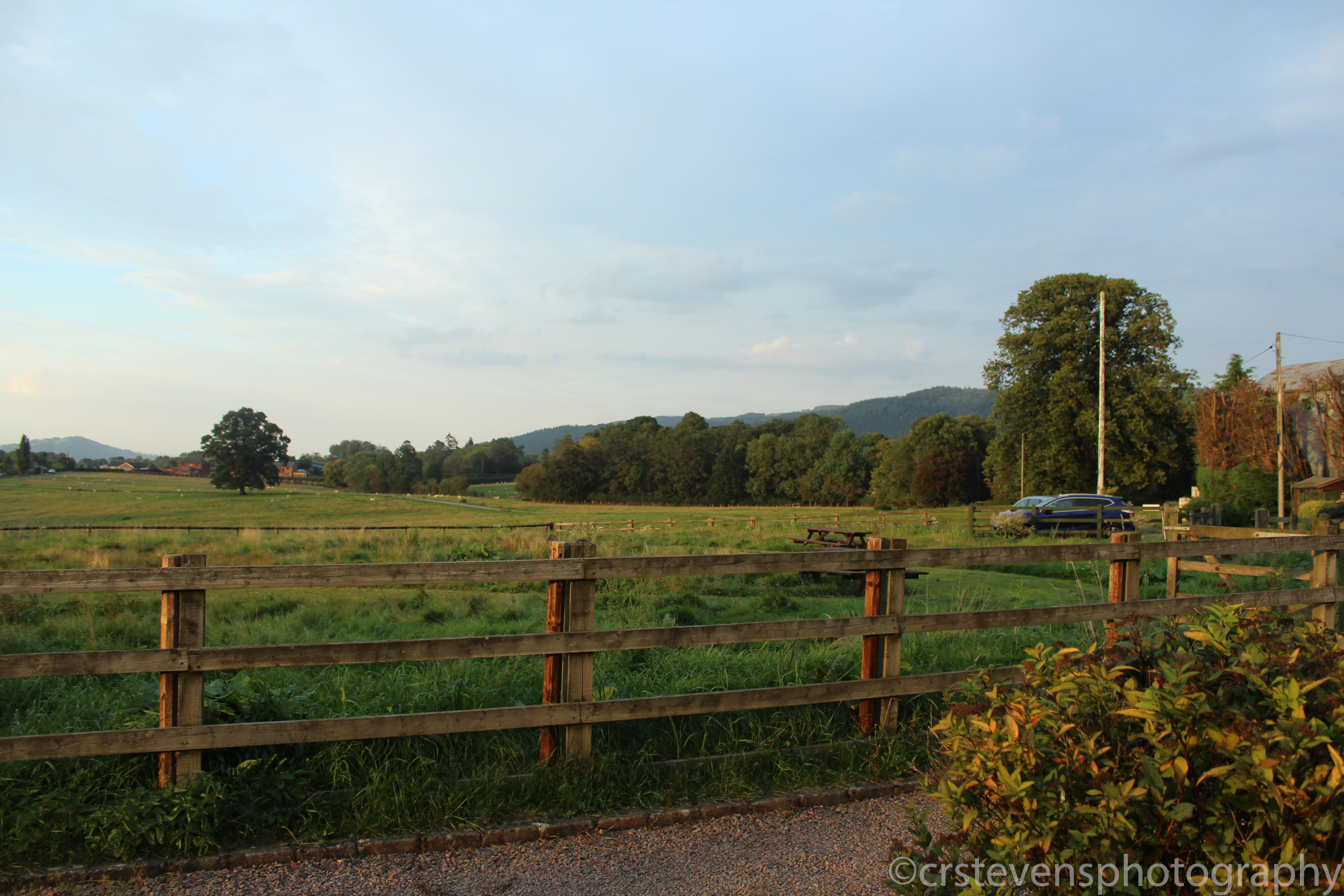 a fence with a field behind it and some trees in the background and some hills further in the background