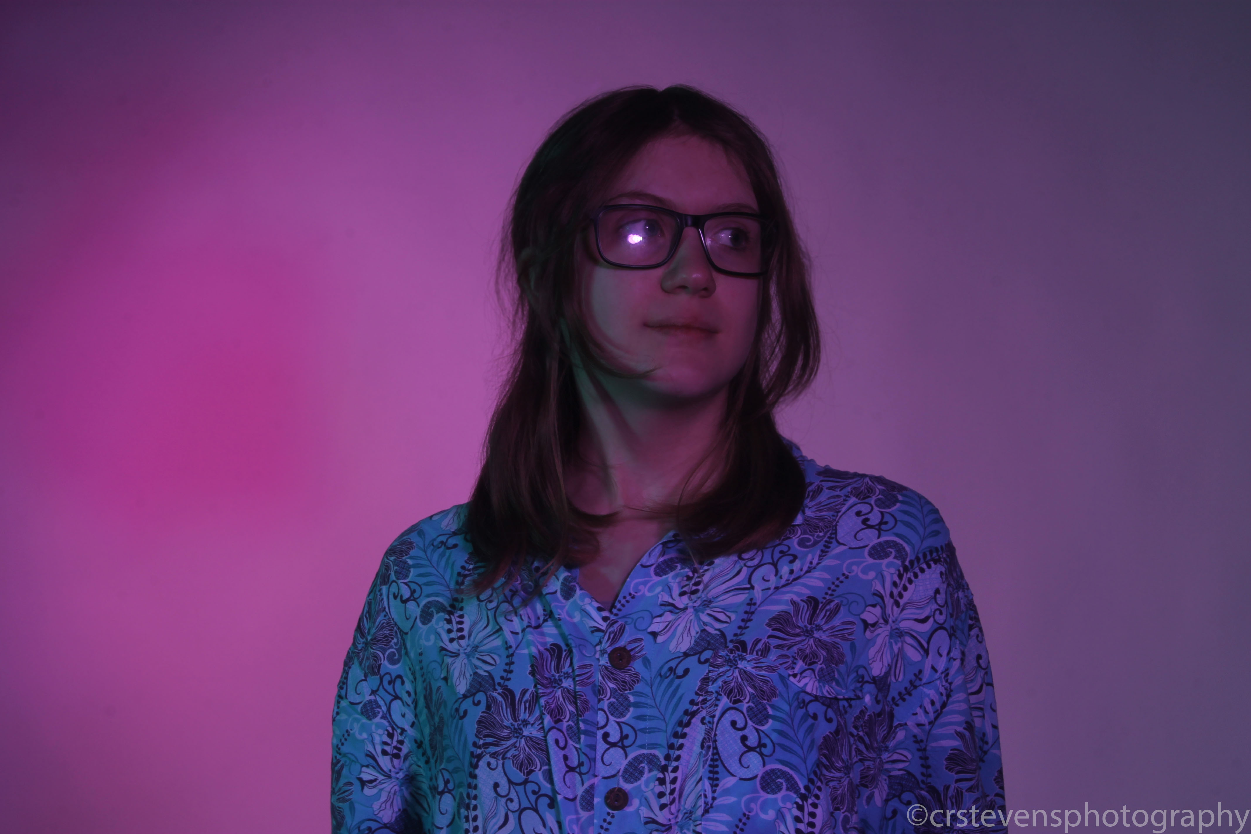 a person with a patterned shirt and glasses looking the side in bisexual lighting