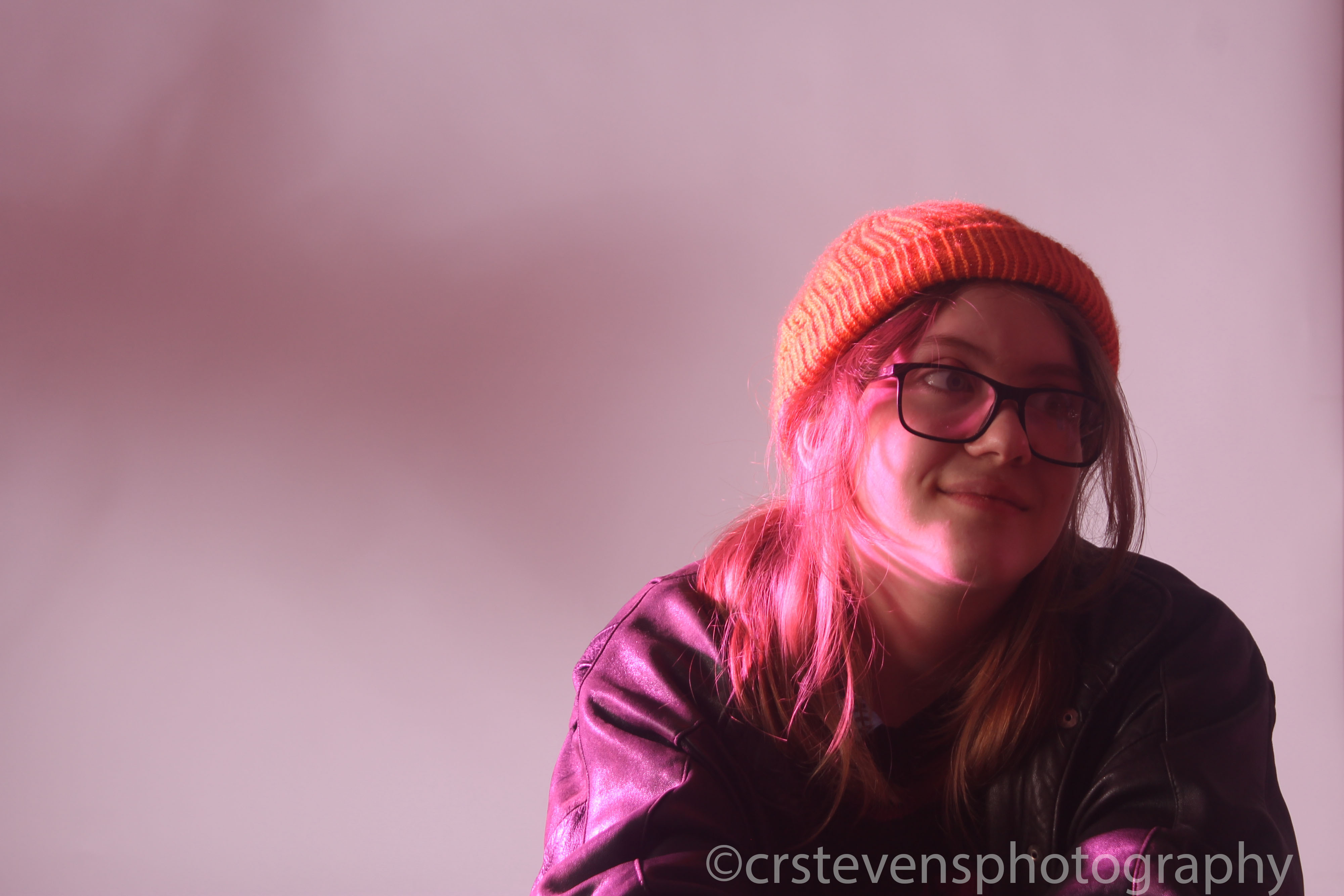 some in a yellow beanie and black jacket looking to the side with pink backlighting